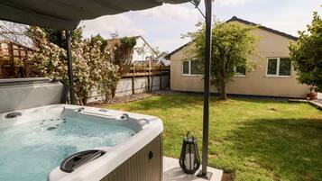 A backyard with a hot tub, a pergola, a potted plant, and a house in the background.