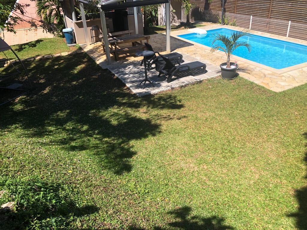 A backyard with a swimming pool, a barbecue area, and a grassy lawn.