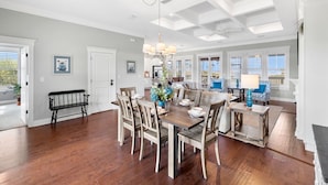 A spacious dining area with a wooden table and chairs, a chandelier, and a view of the outdoors through large windows. - Relax by the Pool, Enjoy Bayfront Views (Port St. Joe)