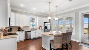 A modern kitchen with white cabinetry, a stainless steel refrigerator, and a large island with bar stools. - Relax by the Pool, Enjoy Bayfront Views (Port St. Joe)