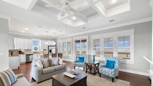 A spacious living room with a grey sofa, a coffee table, and patterned armchairs. A kitchen with white cabinets and a dining area with wicker chairs is visible in the background. - Relax by the Pool, Enjoy Bayfront Views (Port St. Joe)