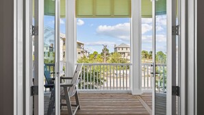 Une terrasse en bois avec une balustrade blanche, une porte vitrée et une vue sur des maisons et des arbres.