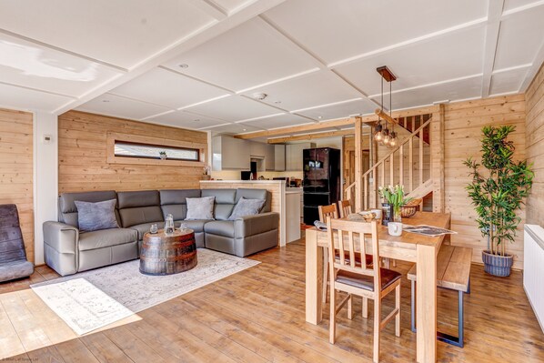 A modern living space with a wooden floor, a grey sofa, a dining table with chairs, and a staircase leading to an upper level.