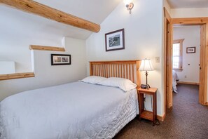 Een slaapkamer met een houten hoofdbord, een nachtkastje met een lamp, en twee ingelijste foto's aan de muur.
