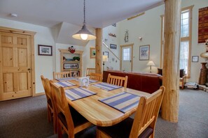 Un coin repas avec une table et des chaises en bois, un luminaire suspendu et une bibliothèque en arrière-plan.