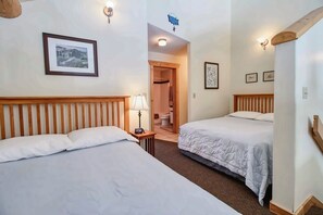 Een hotelkamer met twee bedden, een nachtkastje met een lamp, een lijst aan de muur en een badkamer zichtbaar door een open deur.