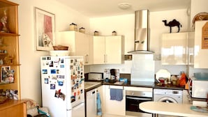 A compact kitchen with white cabinets, a refrigerator covered in photos, a microwave, a stove, and a washing machine. - Appartement T2 Vue Mer (Martigues)