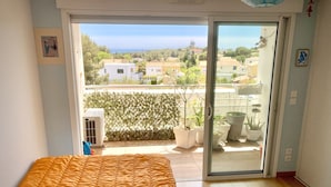 A bedroom with a bed, a sliding glass door to a balcony, and a view of the sea and buildings. - Appartement T2 Vue Mer (Martigues)