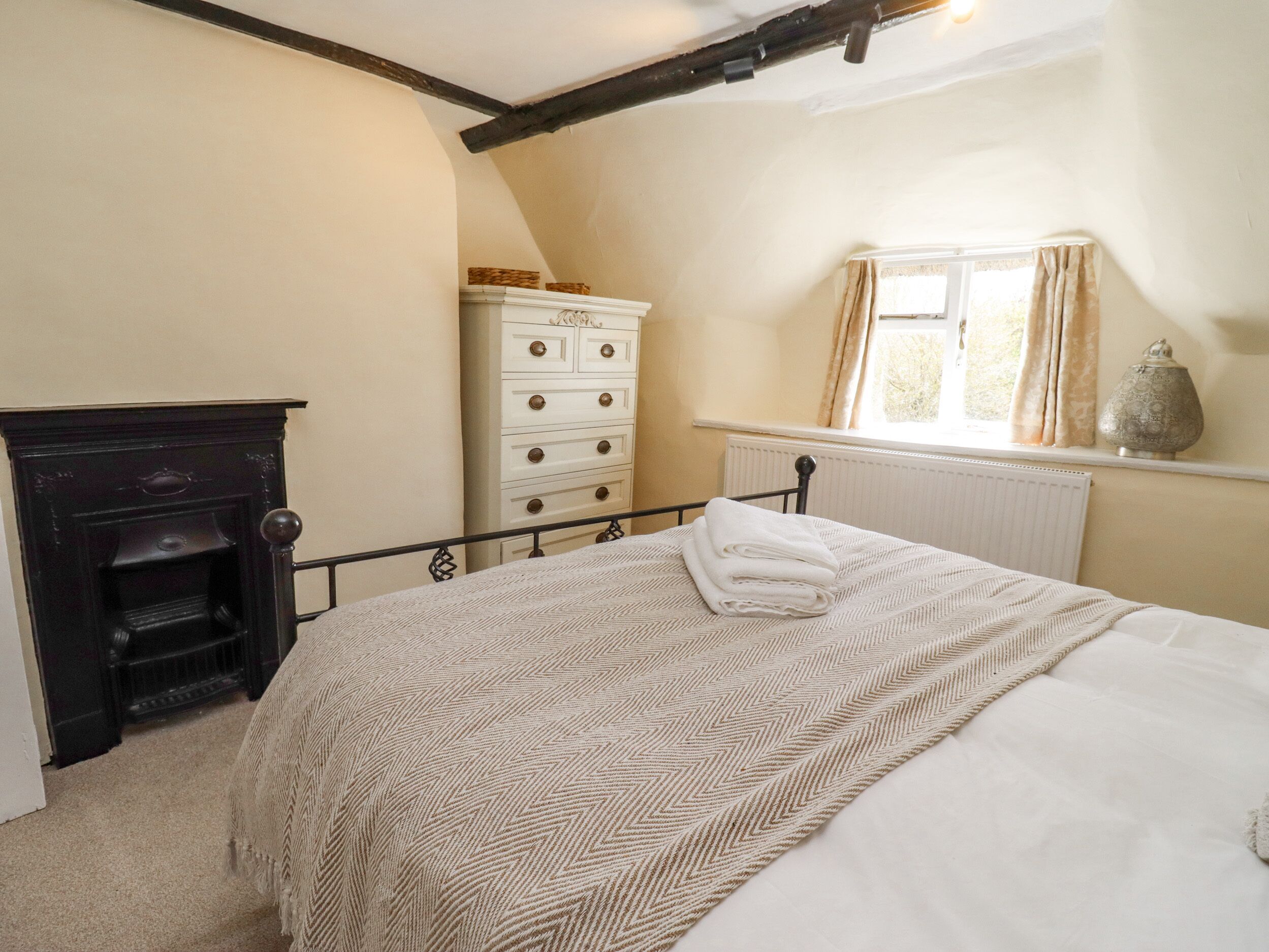 Een slaapkamer met een bed, een dressoir, een radiator en een raam met gordijnen.