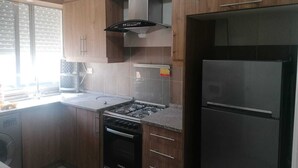 A kitchen with wooden cabinets, a gas stove, a built-in oven, a stainless steel refrigerator, and a window with blinds. - Furnisher apartment in Al Jubiha (Amman)