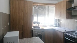 A compact kitchen with wooden cabinets, a washing machine, a microwave, and a stove. - Furnisher apartment in Al Jubiha (Amman)
