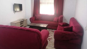 A living room with a red sofa set, a coffee table, and a TV mounted on the wall. - Furnisher apartment in Al Jubiha (Amman)