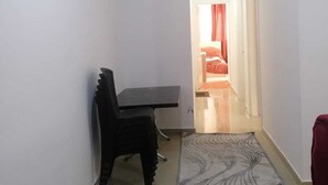 A narrow hallway with a dining area featuring a dark wooden table and chairs, leading to a bedroom with a red bedspread. - Furnisher apartment in Al Jubiha (Amman)