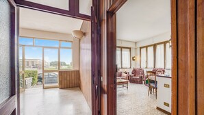 Ein geräumiger Raum mit großem Fenster, einer Holztür und einem Fliesenboden.