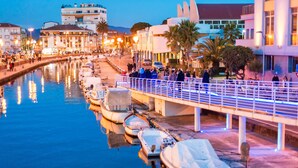 Eine Uferpromenade mit vertäuten Booten, eine Fußgängerbrücke und Gebäude im Hintergrund.