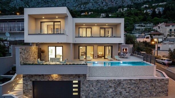 A modern two-story house with a swimming pool, stone facade, and a view of a mountainous area.