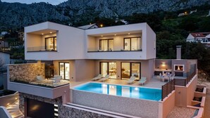 A modern two-story house with a swimming pool, outdoor seating, and a stone facade.