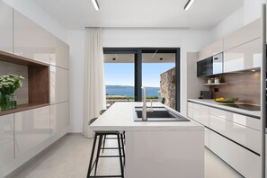 A modern kitchen with a central island, a view of the sea, and a stone wall.