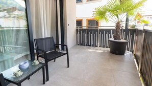 Un balcon avec une chaise, une table avec un bol et une tasse, et un palmier en pot.