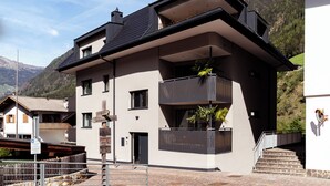 Un bâtiment moderne à deux étages, doté d’un balcon, d’un escalier menant à l’entrée et surplombant un paysage montagneux.