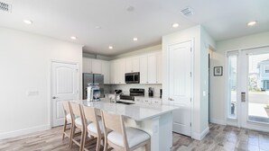 A modern kitchen with white cabinets, a central island with bar stools, stainless steel appliances, and a view of the outside. - Relaxing Margaritaville - Townhome (Kissimmee)