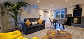 A modern living room with a sofa, a dining table, chairs, and a kitchen area with appliances.
