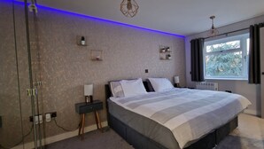 Une chambre à coucher comprenant un lit, des tables de chevet, une fenêtre avec des rideaux et une étagère fixée au mur.