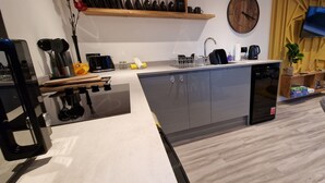 Une cuisine moderne équipée d’un lave-vaisselle encastré, d’un évier et d’un four à micro-ondes. Une étagère en bois se trouve au-dessus de l’évier et un téléviseur est fixé au mur.