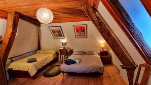 Una camera da letto mansardata accogliente con due letti, travi in legno, una lampada a sospensione e un poster con vista sulla città.