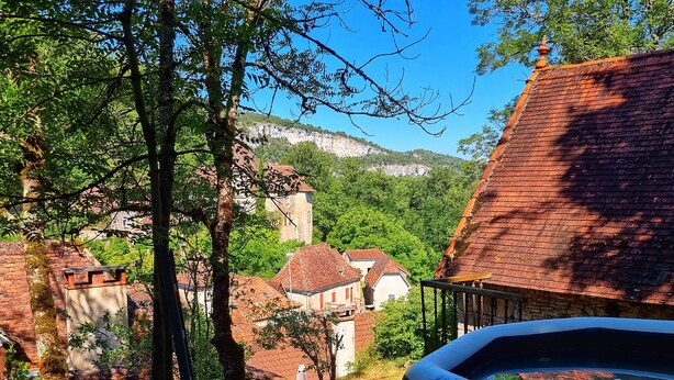 Un borgo rustico con edifici tradizionali, un muro in pietra e vista su una collina con una torre.
