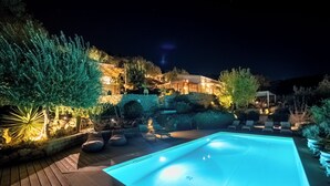 A swimming pool with a wooden deck, surrounded by lounge chairs and a well-lit garden area at night. - Azalo Country House (Avola)