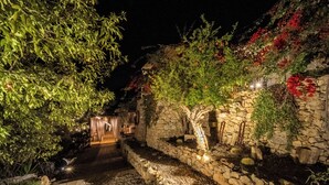 A stone pathway leading to a rustic building with a wooden door, surrounded by greenery and illuminated by ambient lighting. - Azalo Country House (Avola)