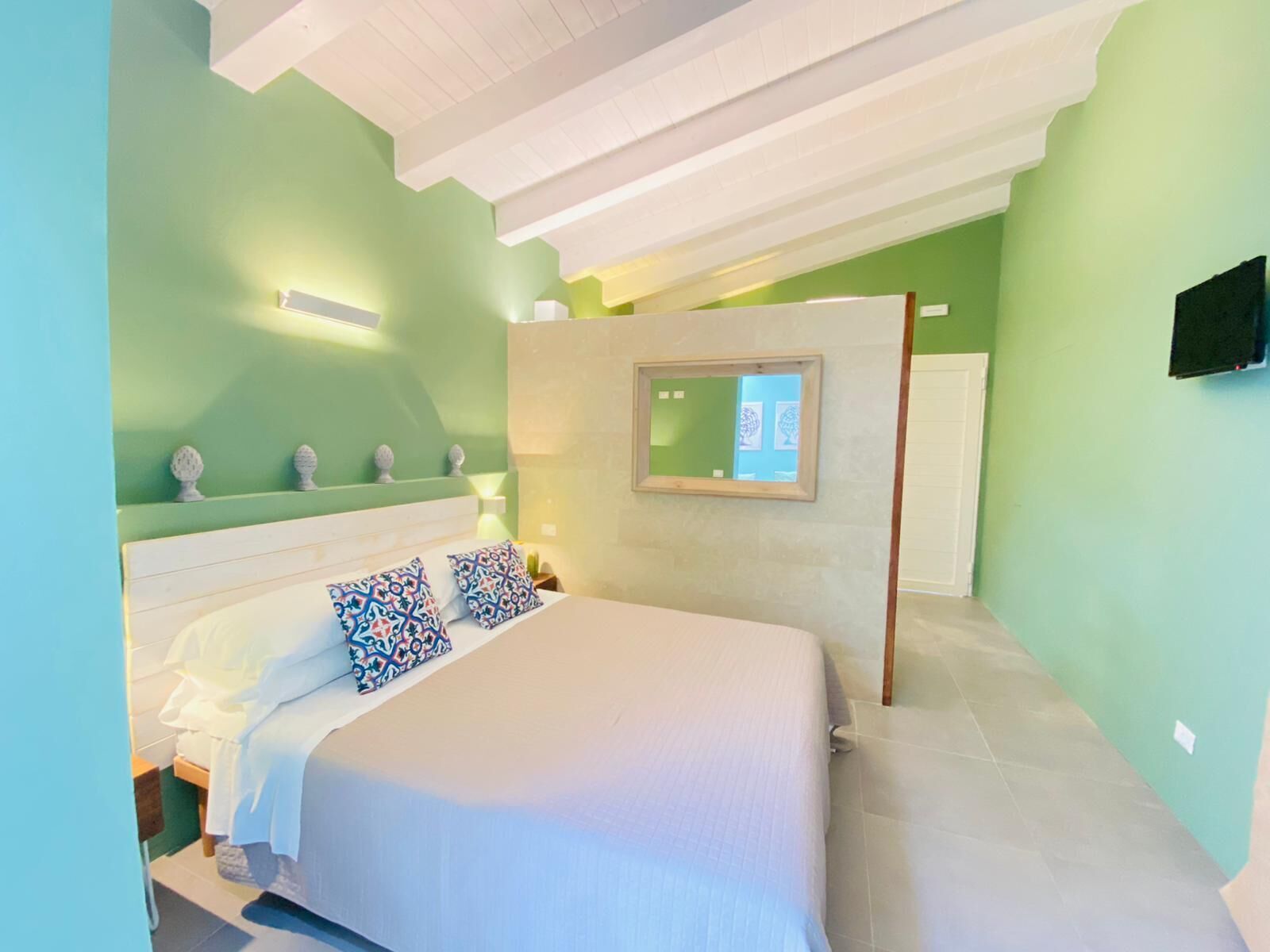 A bedroom with a bed, a bedside table, a mirror, and a television on the wall.