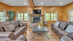 A spacious living room with wooden walls, a stone fireplace, leather sofas, and a flat-screen TV. - Heavenly Views - Amazing Mountain Views 8 Bedroom Cabin by Heavenly Views Resort (Gatlinburg)