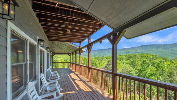 A wooden deck with white plastic chairs and a view of green mountains. - Heavenly Views - Amazing Mountain Views 8 Bedroom Cabin by Heavenly Views Resort (Gatlinburg)