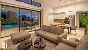 Una sala moderna con un juego de sofá, una mesa de comedor con sillas, una zona de cocina y un amplio ventanal corredero que da a un espacio exterior.