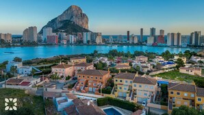 Un paisaje costero con una montaña destacada al fondo, edificios residenciales con balcones visibles y una vista despejada del mar.