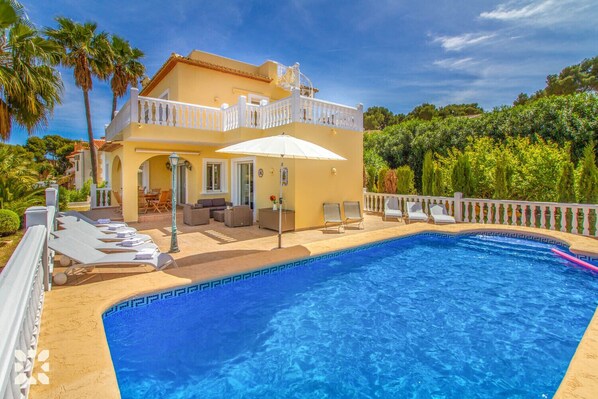 A two-story house with a swimming pool, outdoor seating, and a white fence.