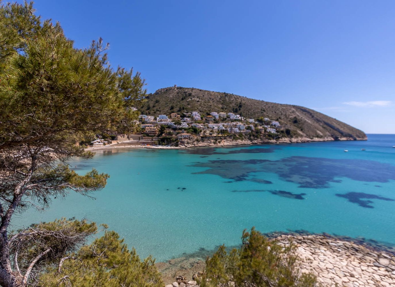 A coastal town with houses on a hillside overlooking a clear blue sea.