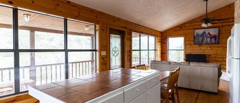 A kitchen with wooden walls, large windows, a white countertop, and a dining area with a sofa.