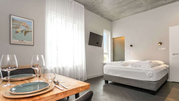 Quarto de hotel com uma cama, uma mesa de jantar com pratos e copos, um quadro na parede e uma TV fixada na parede.