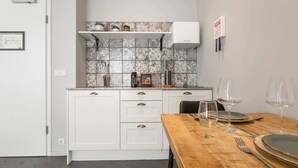 Cozinha moderna com armários brancos, painel de azulejos e área de jantar com mesa de madeira posta para dois.
