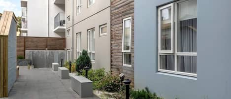 A modern residential building with a narrow courtyard, concrete benches, and a small garden area.