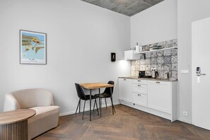A compact kitchen with a herringbone floor pattern, white cabinetry, and a small dining area with a wooden table and black chairs. - Swan Double Studio for 2 (Reykjavík)