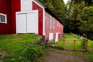 Punainen rakennus, jossa on valkoiset ovet ja ikkunat, ja sen ympärillä on vehreää kasvillisuutta sekä puinen aita.