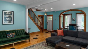 Una sala de estar con una escalera, un sofá verde, un sofá oscuro y una mesa de centro de madera.