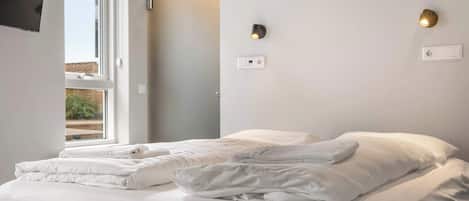 A hotel room with a bed, two wall-mounted light fixtures, and a window.