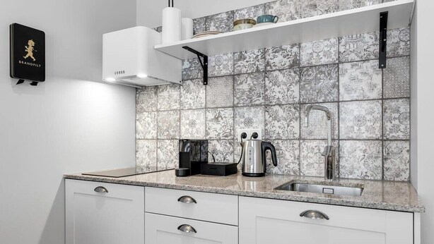 Et køkken med hvide skabe, en stålvask og et mønstret bagpanel.