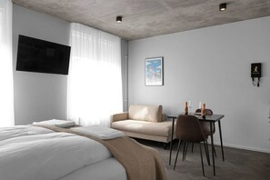 Een hotelkamer met een bed, een bank, een tafel met twee stoelen, een flatscreen-tv aan de muur en een lijst met een afbeelding.