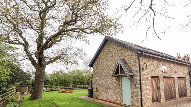 Un bâtiment en briques avec une porte verte, un panier de basket et un grand arbre au premier plan.